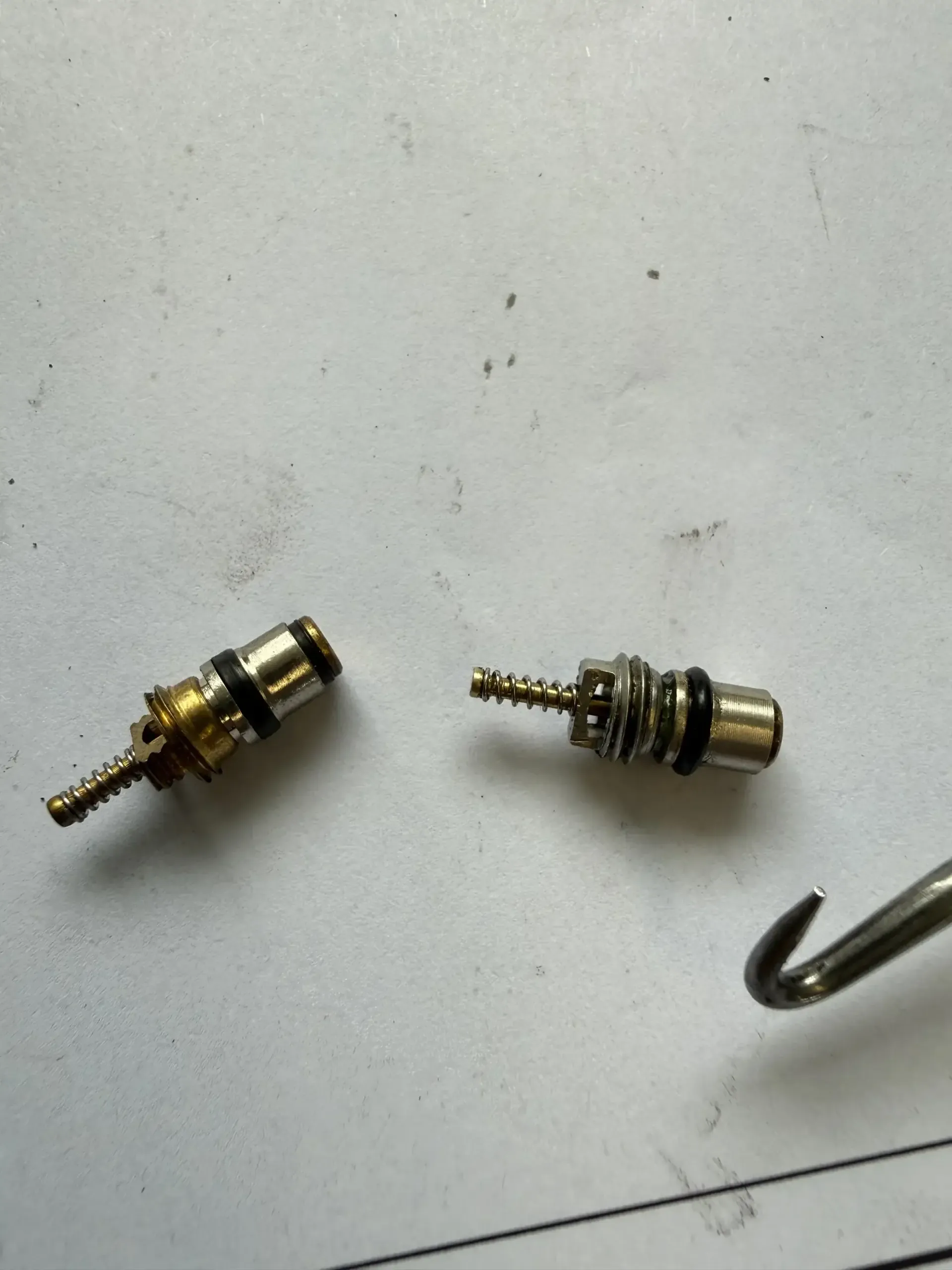 Old vs new AC service-port valve cores side by side at Beacon Auto Care San Mateo