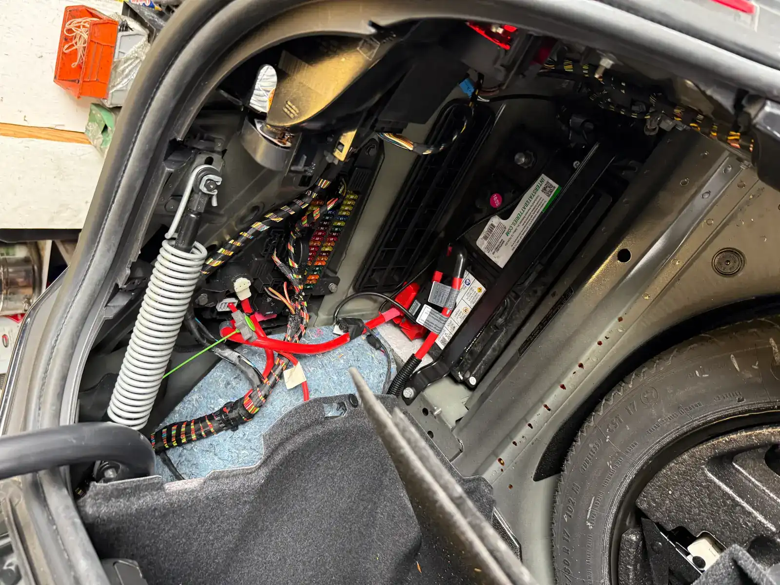 Trunk-mounted European-style battery in the side compartment, wiring harness and fuse box visible during a battery replacement at Beacon Auto Care San Mateo